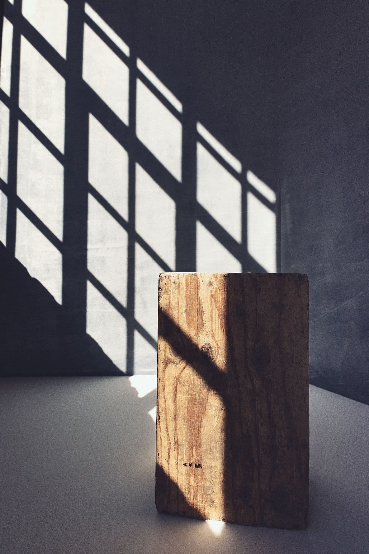 Ein Holzblock im Schattenraster eines Sprossenfensters