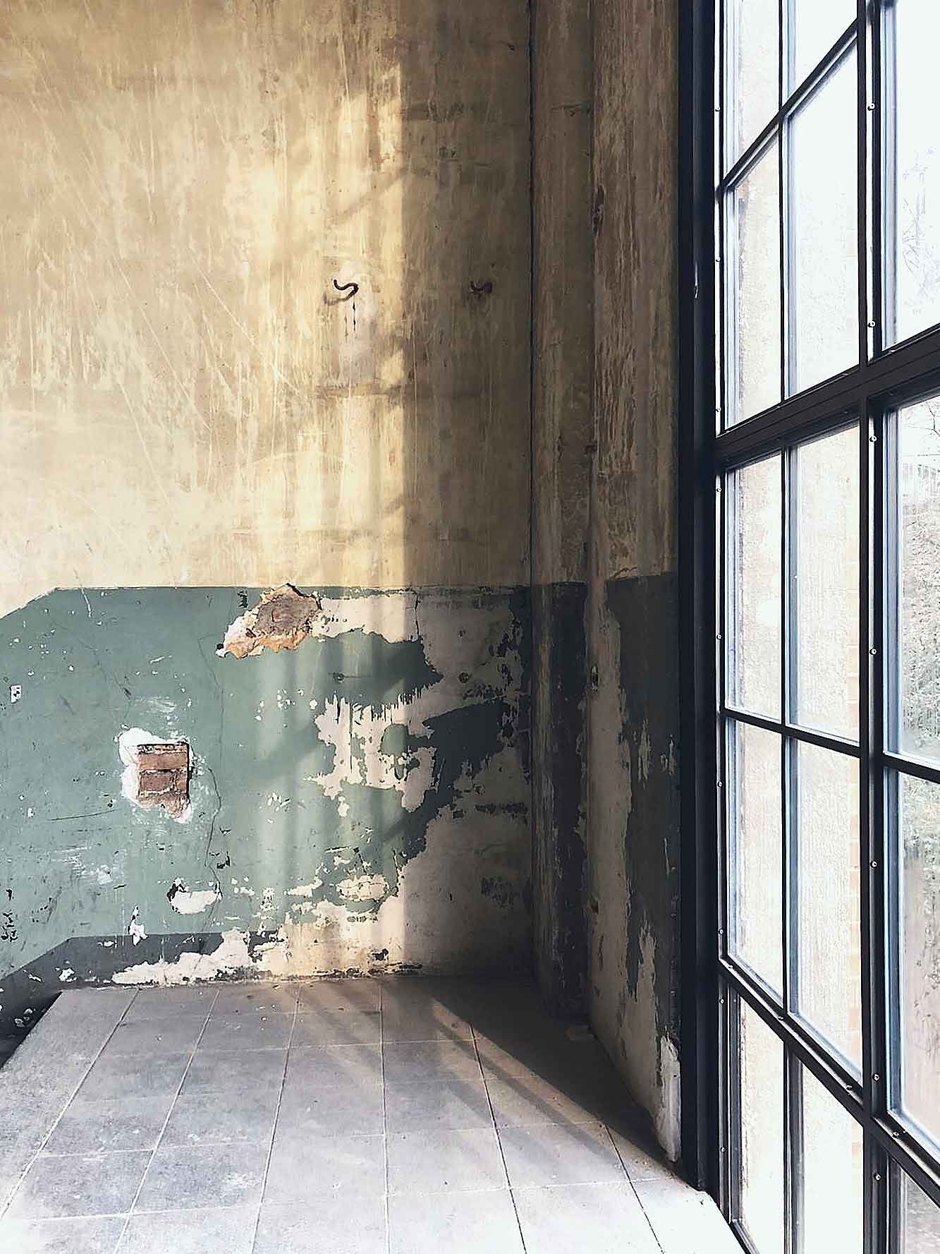 Abgeblätterte Wandfarbe und Fliesenboden neben einem hohen Sprossenfenster